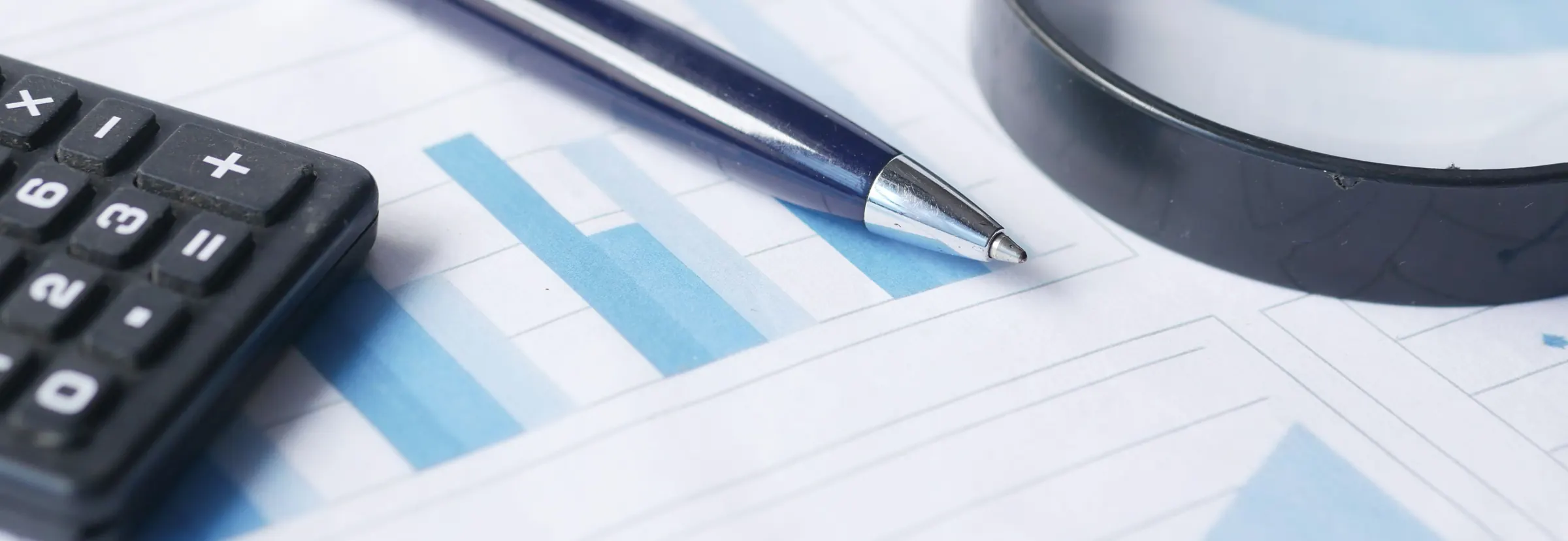 A calculator, a pen and a magnifying glass on a printed bar chart in shades of blue