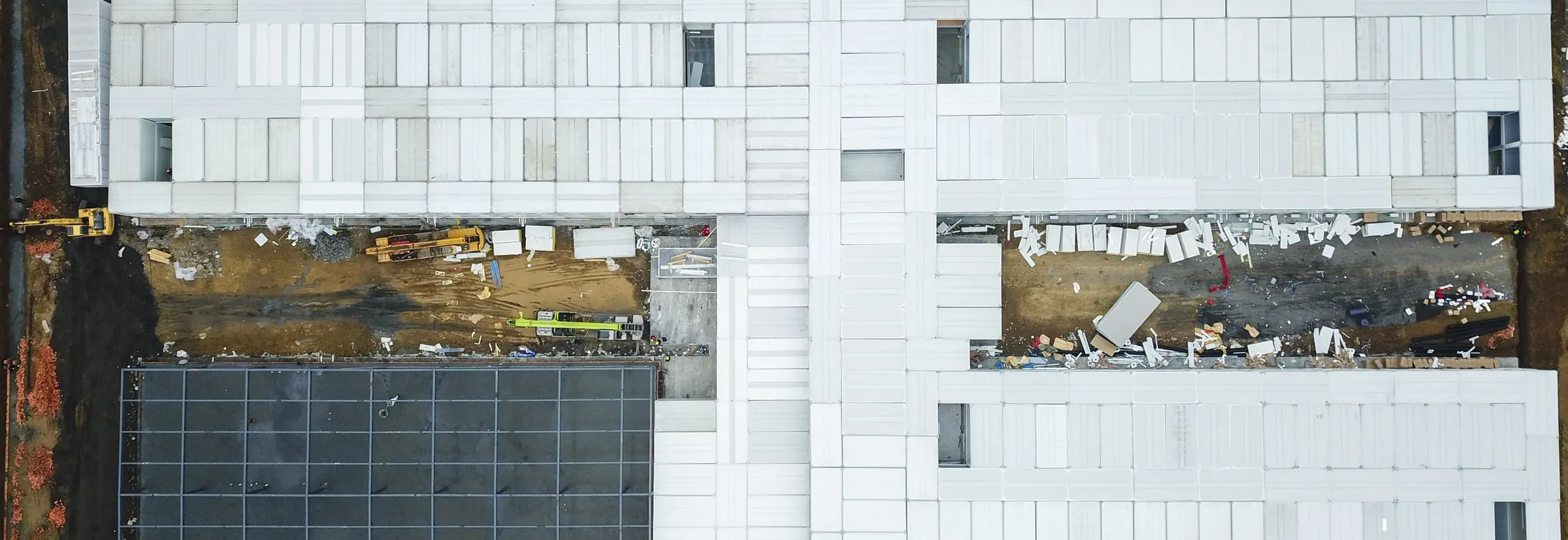 Aerial view of an unfinished building complex, with debris and construction machines in the gaps between the roofs