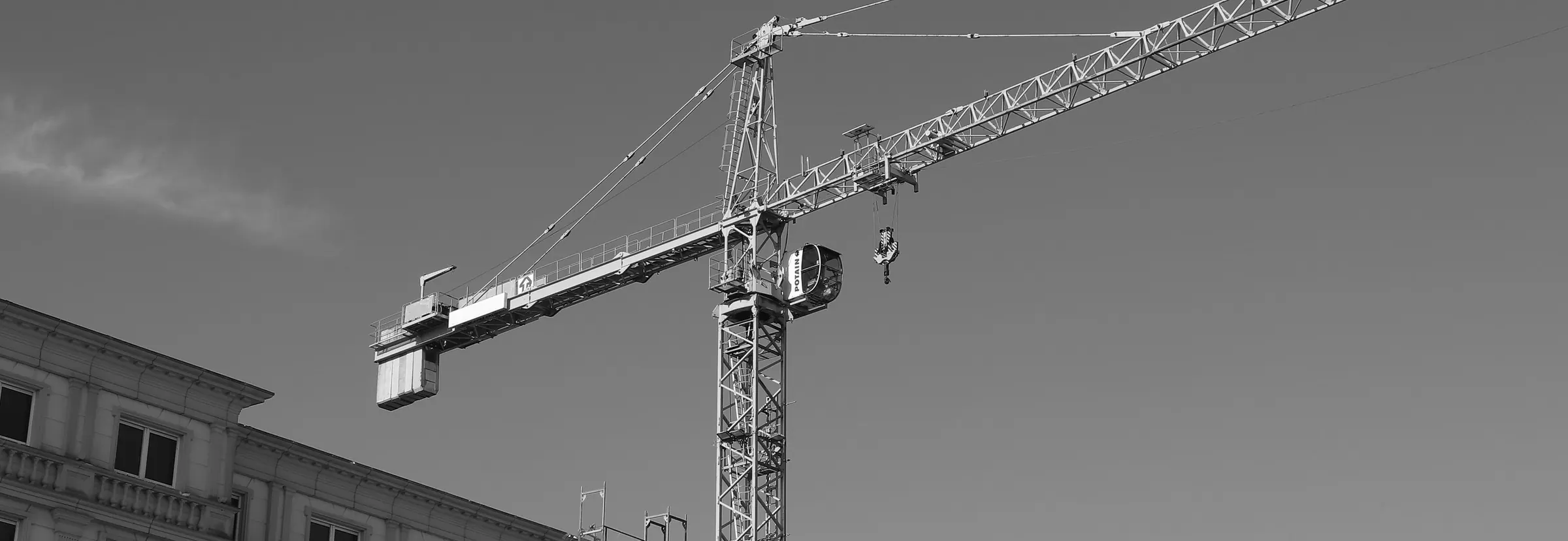 A tower crane against the sky over the edge of an old stone building, in black and white