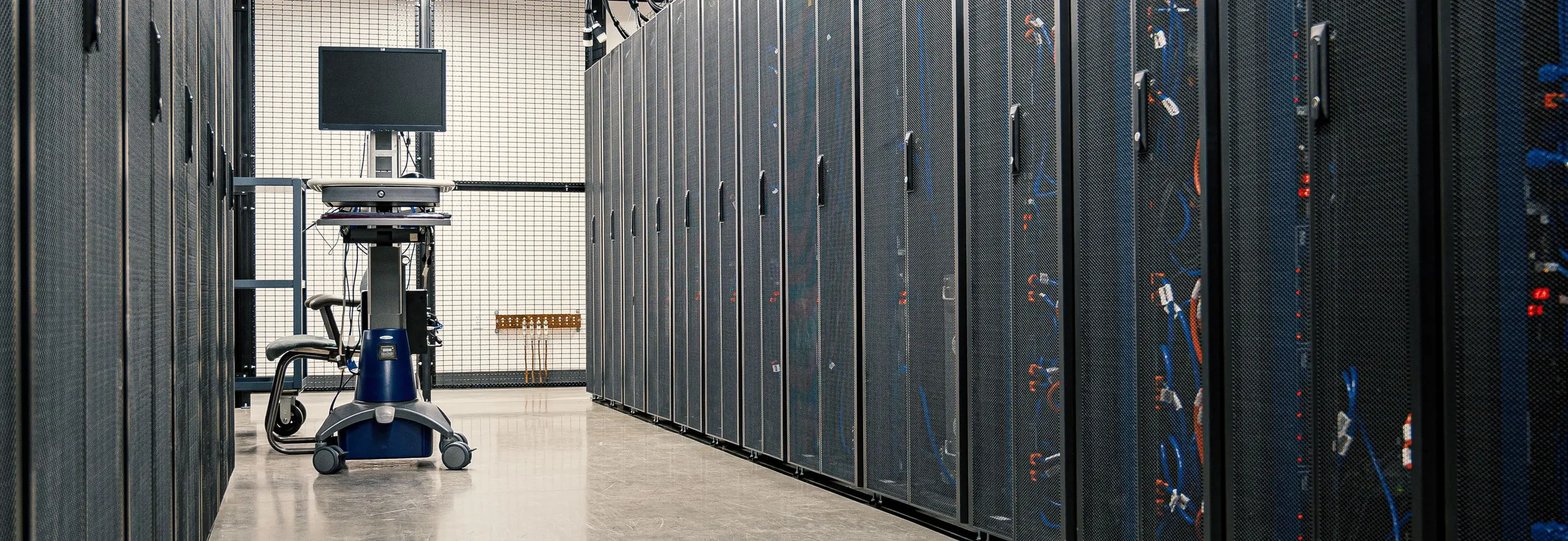 An aisle between rows of server racks in a data center, with a workstation cart at the far end