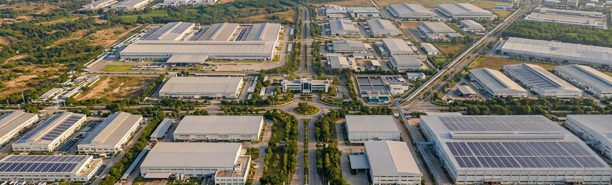 Aerial view of an industrial estate, factory roofs lined with solar panels either side of a central road, with hills behind