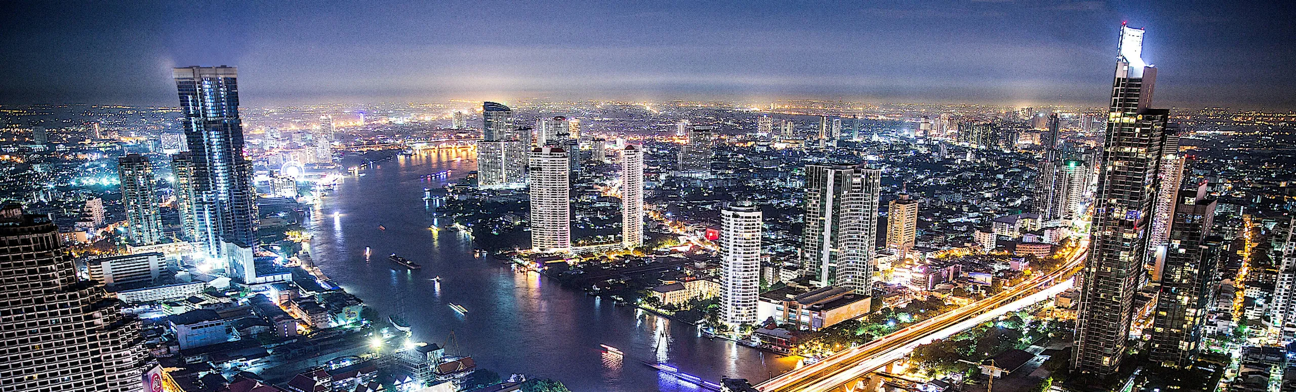 The Chao Phraya River winding through Bangkok at night, lined with lit high-rise towers