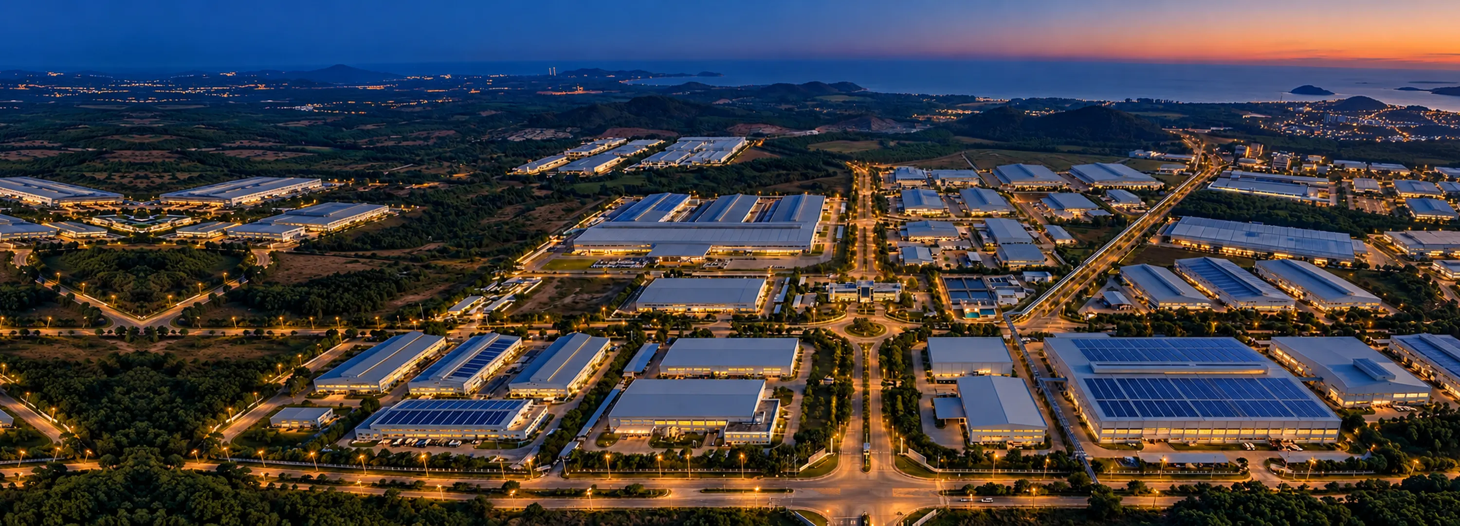 Aerial view of an industrial estate, factory roofs lined with solar panels either side of a central road, with hills behind