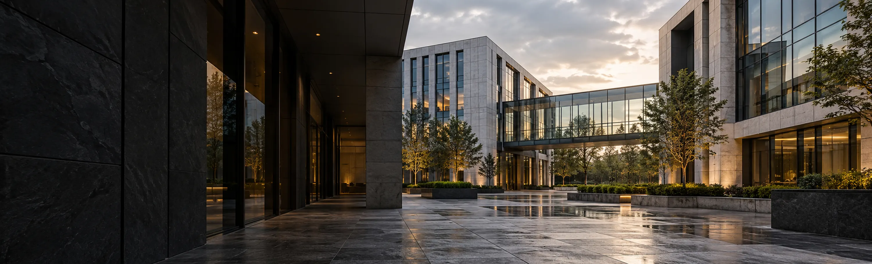 An office campus at golden hour, glass buildings joined by skybridges around a landscaped courtyard