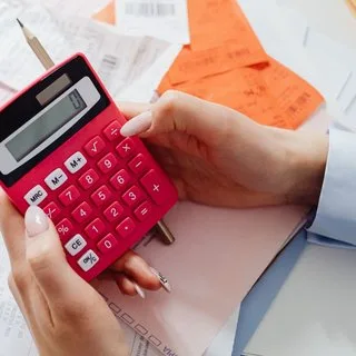 Hands using a red calculator over printed financial papers
