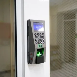 A fingerprint scanner and keypad access terminal on a wall beside a glass door